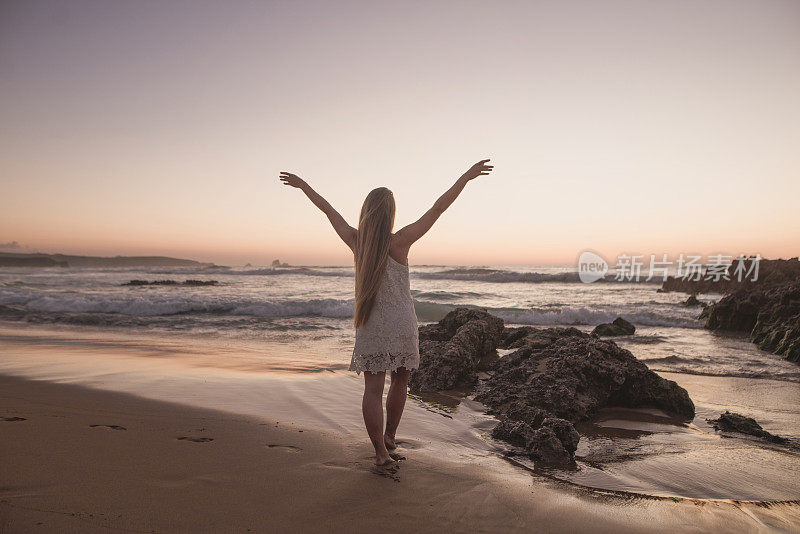 年轻的女人在海边举起双手