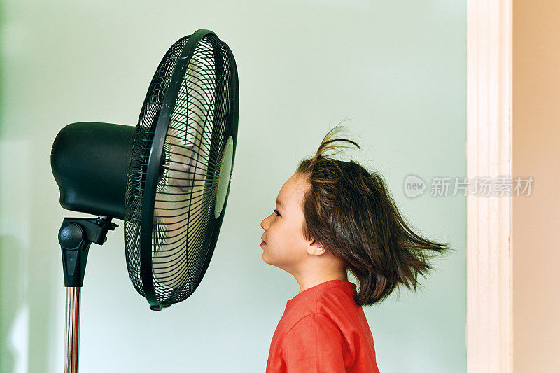 在炎热的夏日里，可爱的孩子站在电风扇前