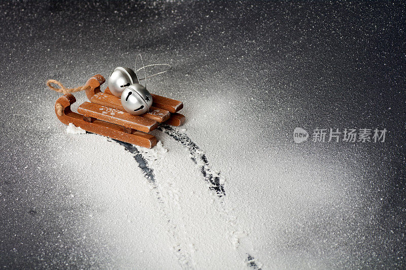 木制的雪橇上放着白色的人造雪，银色的铃铛躺在雪橇上，雪车的轨迹，黑色的背景