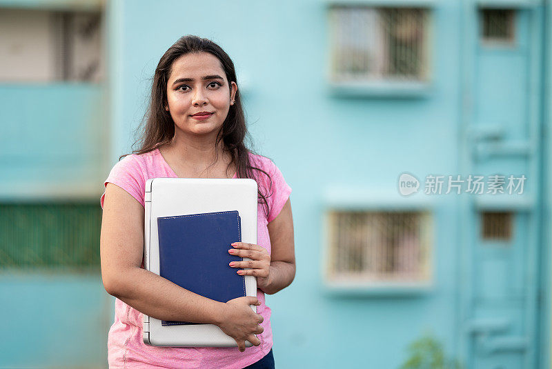 微笑的年轻女大学生与书和笔记本电脑