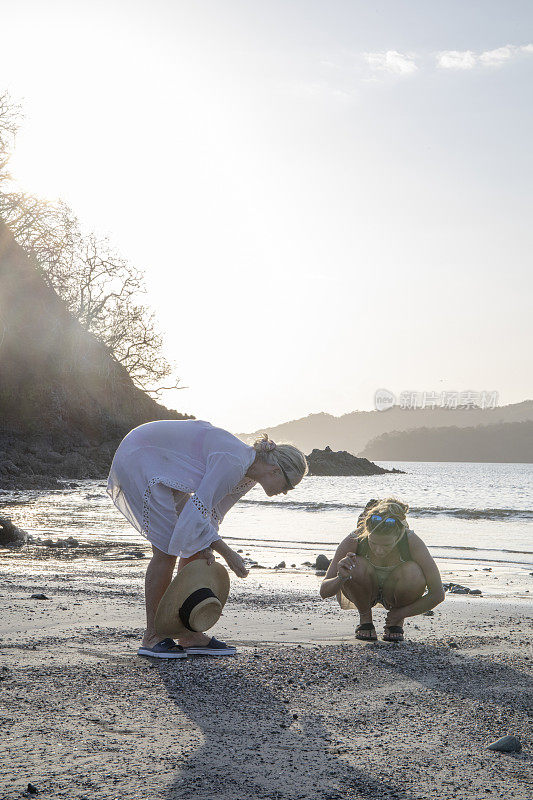 妈妈和女儿早上在海滩上寻找贝壳