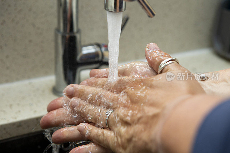 一个女人的手正在厨房水槽的自来水下清洗的特写