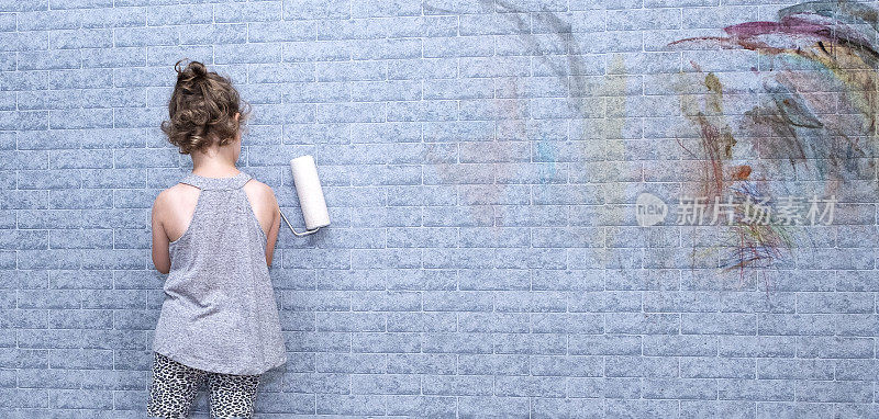 一个6岁的白人女孩在墙上画画。小女孩手里拿着一个油漆滚筒。