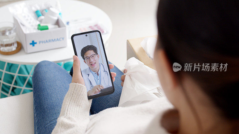 肩观年轻的亚洲妇女与医生在手机视频会议医疗应用程序在远程医疗在线服务医院隔离社会距离在家的概念。