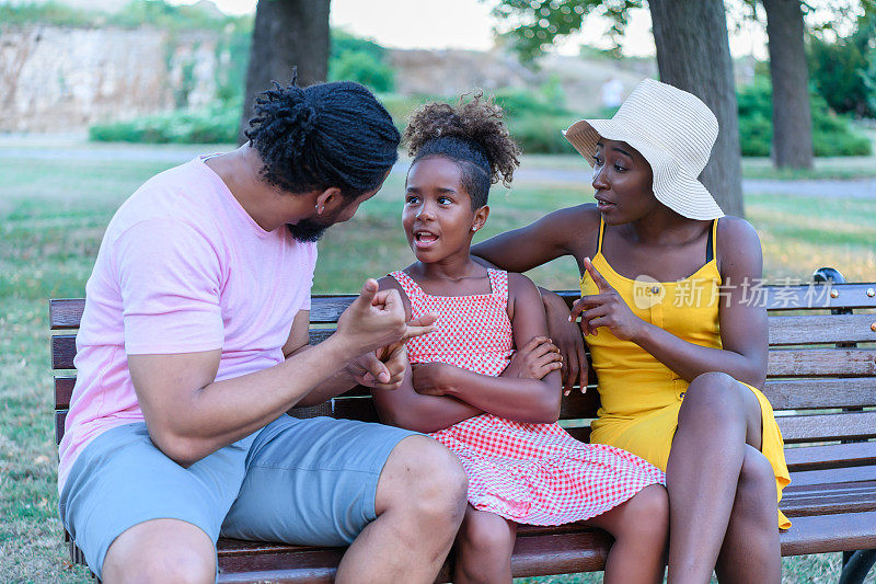 一个非洲家庭坐在公园长椅上，讨论家庭问题。