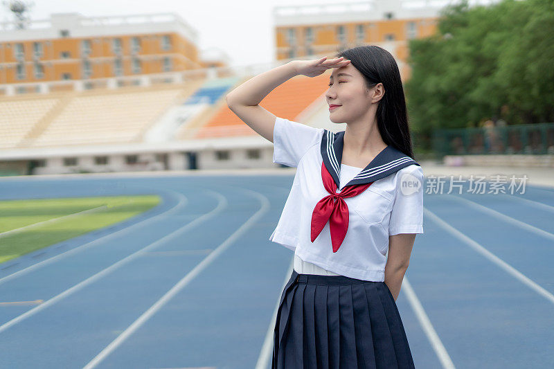 身穿白色制服的年轻亚洲女性在大学操场上锻炼、跑步和散步