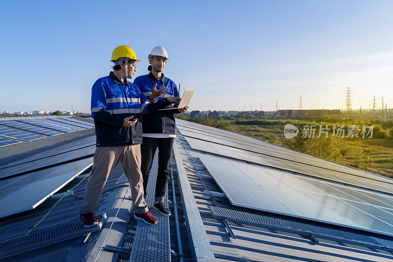 专业技术员专业工程师带着笔记本电脑和平板电脑进行维护检查，在阳光下安装工厂屋顶太阳能电池板。工程师小组调查检查太阳能电池板屋顶。
