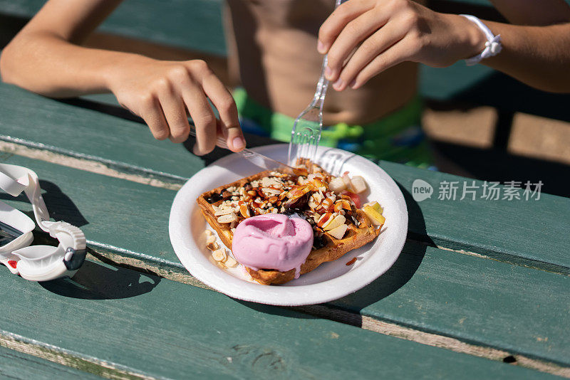 一个小男孩在海滩上吃果酱华夫饼。