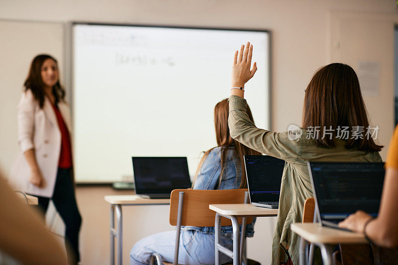 高中信息技术课上学生举手提问的后视图。