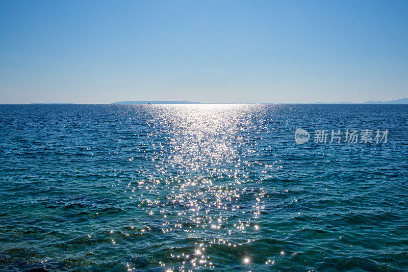 阳光下波光粼粼的大海，背景是克罗地亚的岛屿，蔚蓝的天空