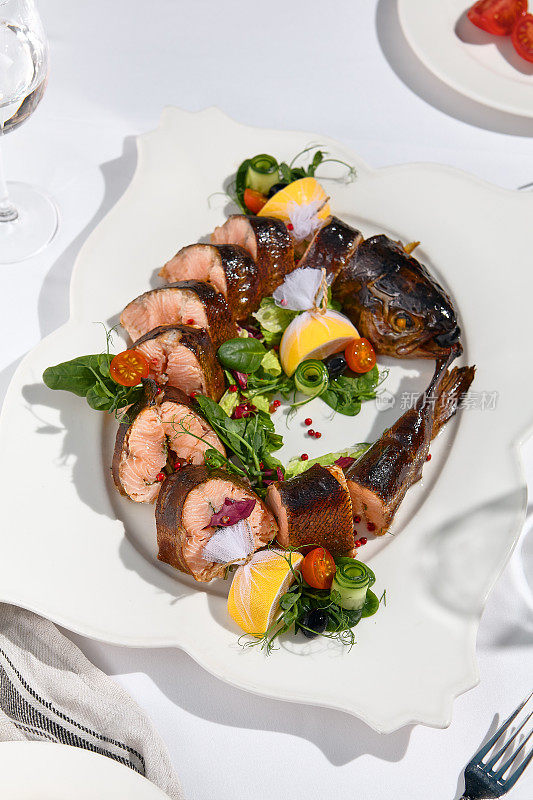 宴会菜肴——白餐桌上的熏虹鳟鱼。优雅的熏鱼鳟鱼，适合晚宴、婚礼、节日聚会。宴会菜单的食物造型。