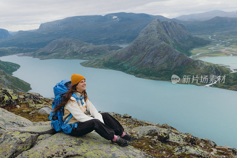 挪威约顿海门国家公园，一名女背包客坐在山顶上凝视着群山的侧视图