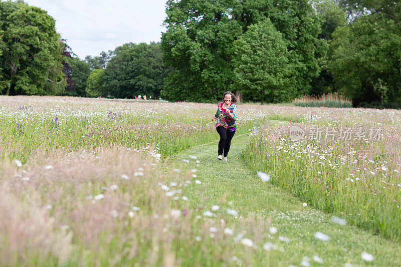 一位年长的妇女在一条小径上跑步，这条小径穿过长满野花的草地
