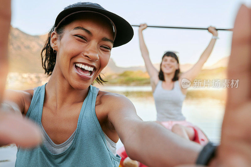 两个微笑的朋友在夏天的时候一起自拍，一起在湖上划皮艇。微笑快乐俏皮的女人在户外与水的活动。