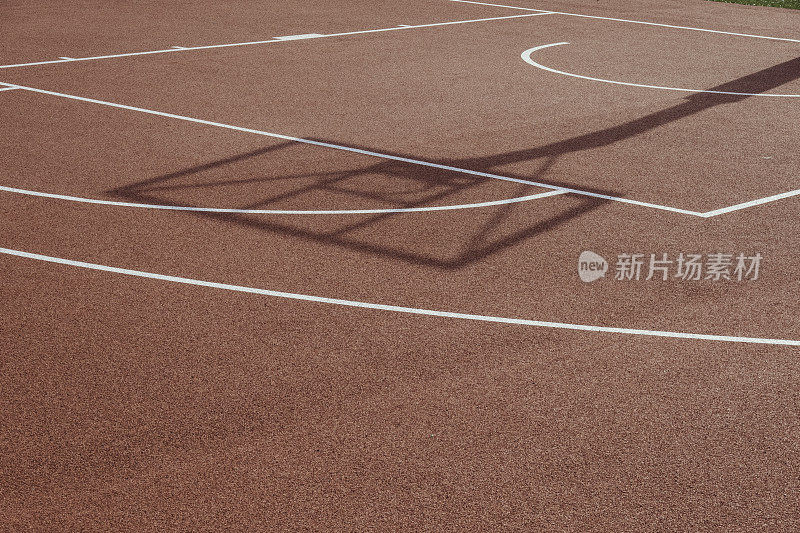 阳光明媚的户外，在橙色的篮球橡胶场上的篮球架和篮球圈的影子。篮球比赛的背景