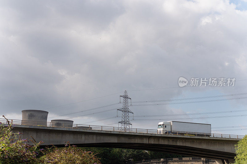 货物运输铰接式卡车行驶在高速公路河桥上，桥上有发电厂和电线的工业背景。用Lensbaby相机拍摄故意模糊