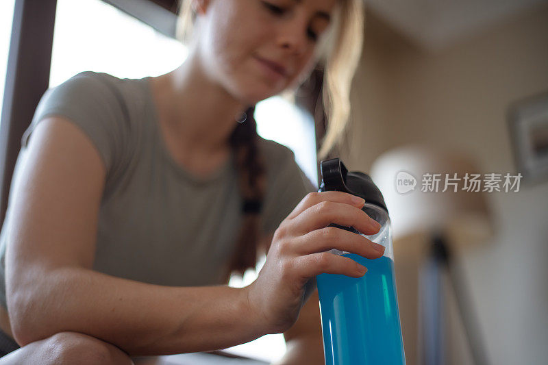 年轻女子在家里的客厅锻炼期间补水。