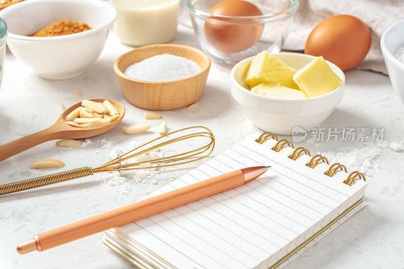 记事本和笔，碗里放着烘焙材料，大理石桌上放着金色打蛋器