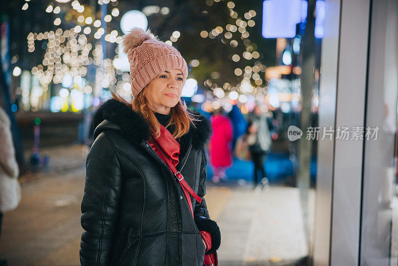 在冬季假期的夜晚，妇女站在灯火通明的城市街道上