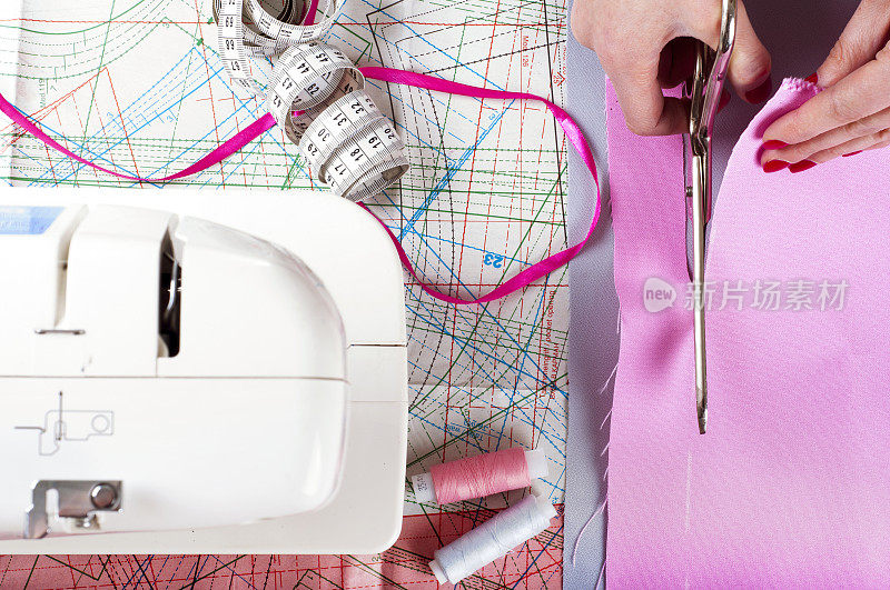 时装设计师的概念。女人的手切割粉红色的织物在工作室。模式的背景