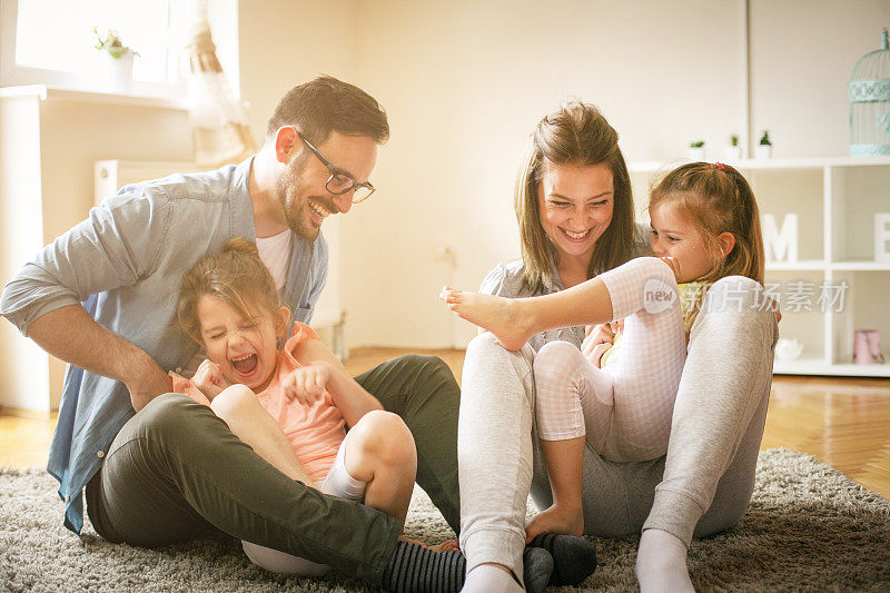 幸福的家庭，两个女儿在家里玩。一家人坐在地板上一起玩。
