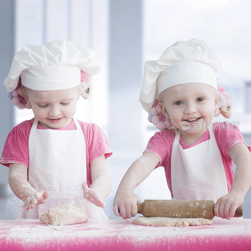 两个小女孩穿着白色围裙，戴着厨师帽烘焙