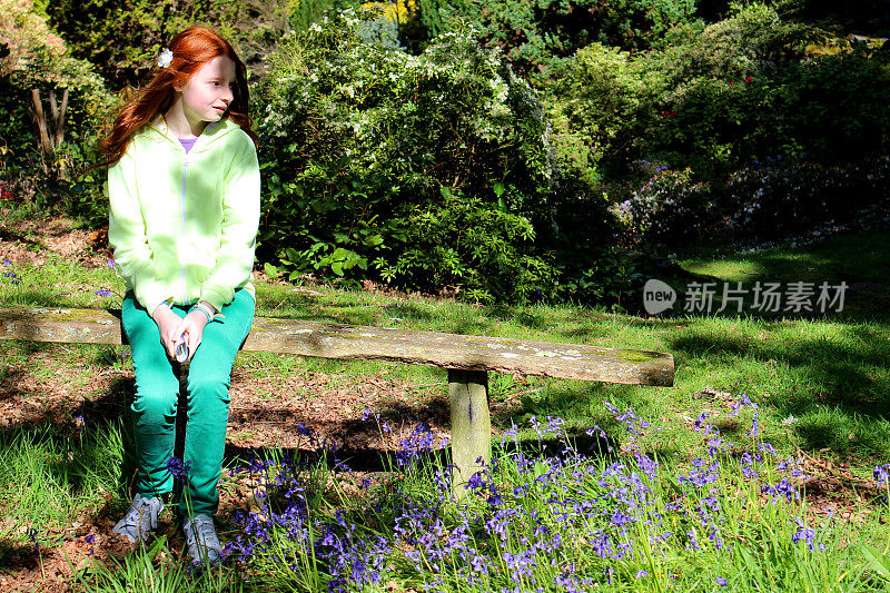 女孩坐在长满森林风信子的质朴的花园木凳上