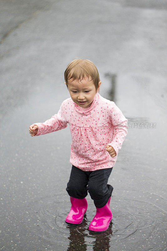 穿着雨靴在水坑里跳的小女孩