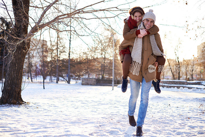 在冬季公园里，快乐的男人背着他可爱的女朋友
