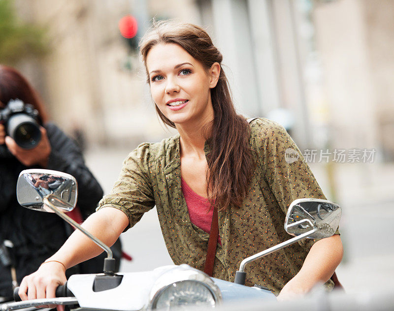 一个女人正在给一个骑摩托车的女孩拍照。