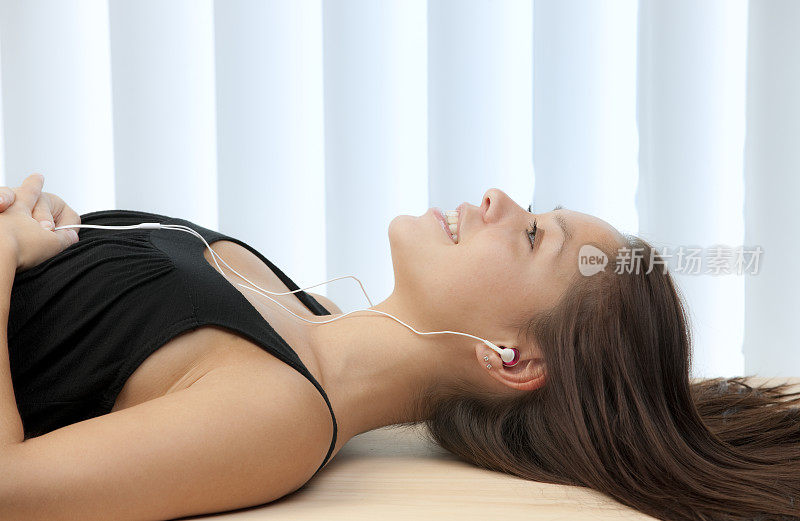 年轻女子仰面躺着，戴着耳机听着音乐