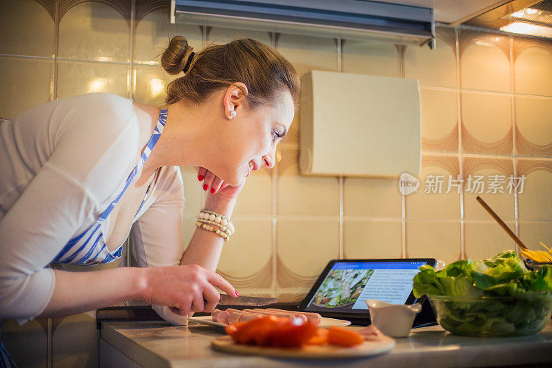 美丽的年轻女子在数字平板电脑上阅读食谱