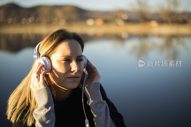 戴着耳机的女人在湖边码头上听音乐