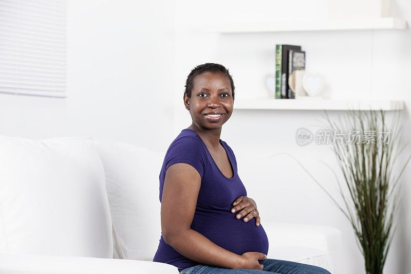 坐在沙发上的快乐怀孕的非洲裔美国女人