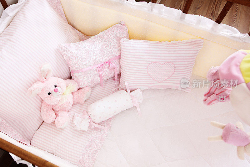婴儿床有粉色的垫子，白色的被子和柔软的兔子