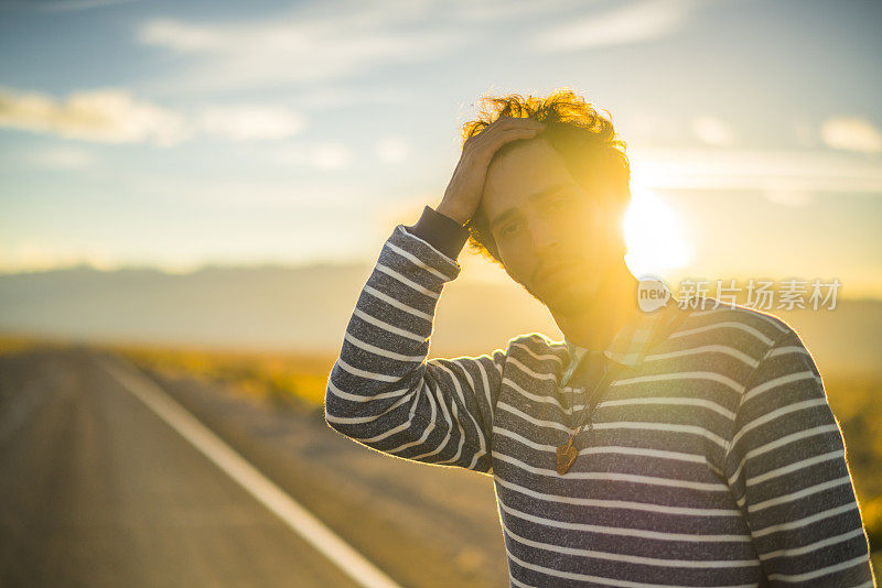 公路旅行。一个年轻人，旅行潮人，在日落时分的内华达州沙漠公路上四处张望