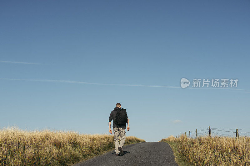 一个背着背包走在偏远乡村路上的人。