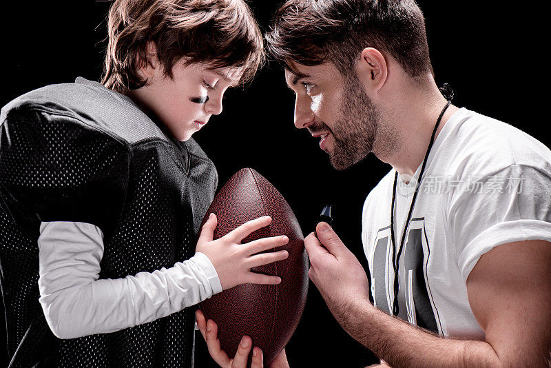 教练和男孩与橄榄球面对面站在黑色的侧视图