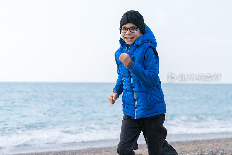 快乐男孩在一个冬日的海滩上慢跑