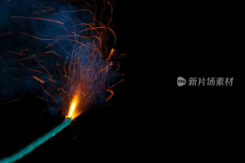 燃烧的引信与火花和蓝色烟雾隔离在黑色背景