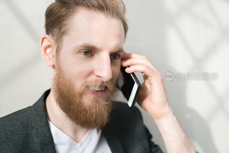 积极自信帅气的潮男经理，留着胡子，一边用手机一边进行重要的谈话