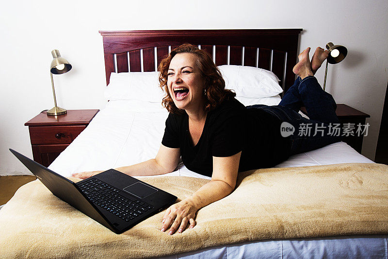 笑着的女人躺在床上，手提电脑