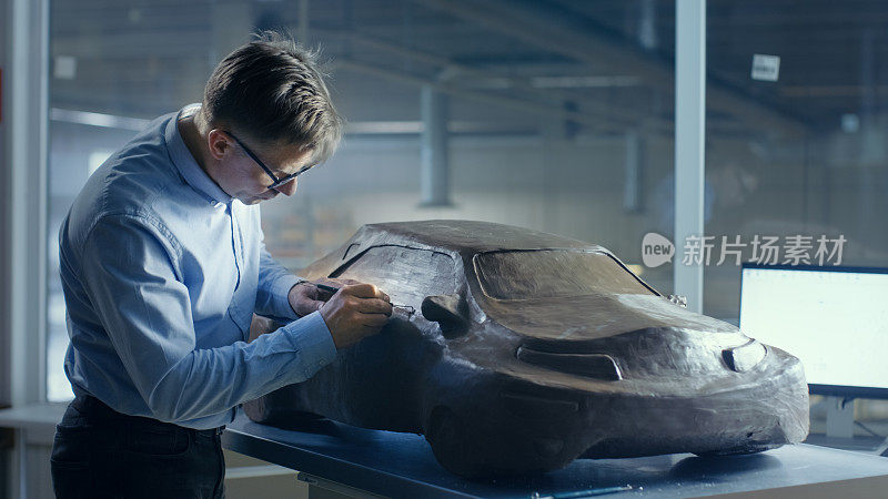 灰色头发的汽车设计师雕刻未来汽车模型从橡皮泥与电线。他在一家大型汽车厂的专门工作室工作。