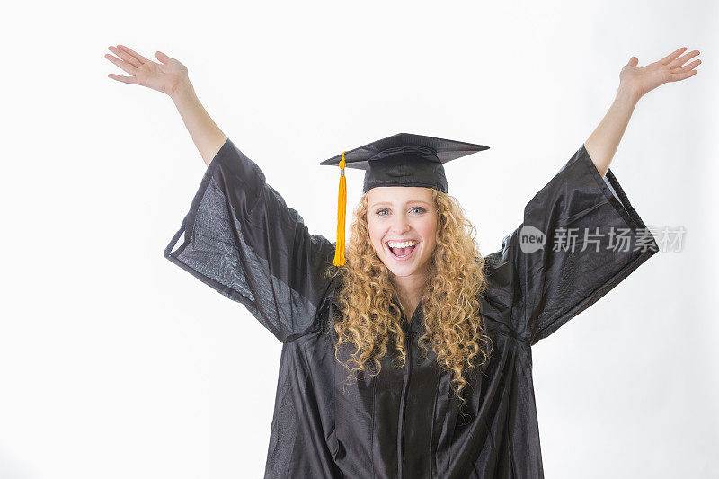 十几岁的女孩戴着毕业帽和礼服兴奋地举起手臂