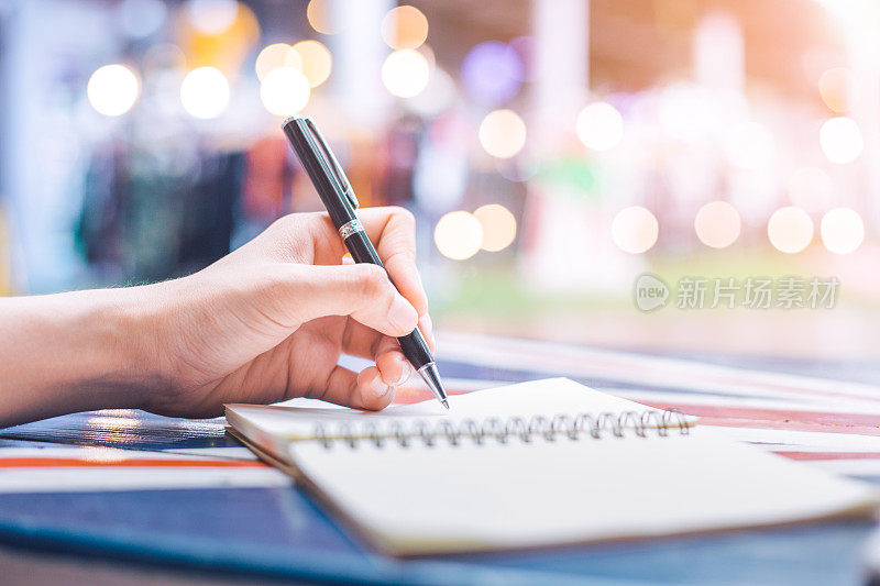 在木桌上用钢笔在笔记本上写字的女人的手。