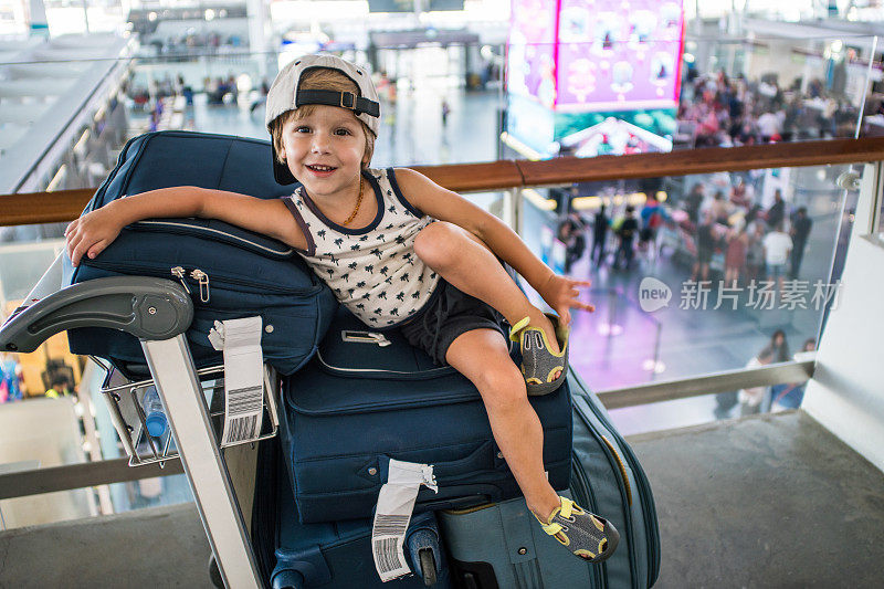 一个戴着帽子的酷男孩在机场等飞机的时候坐在行李箱上。