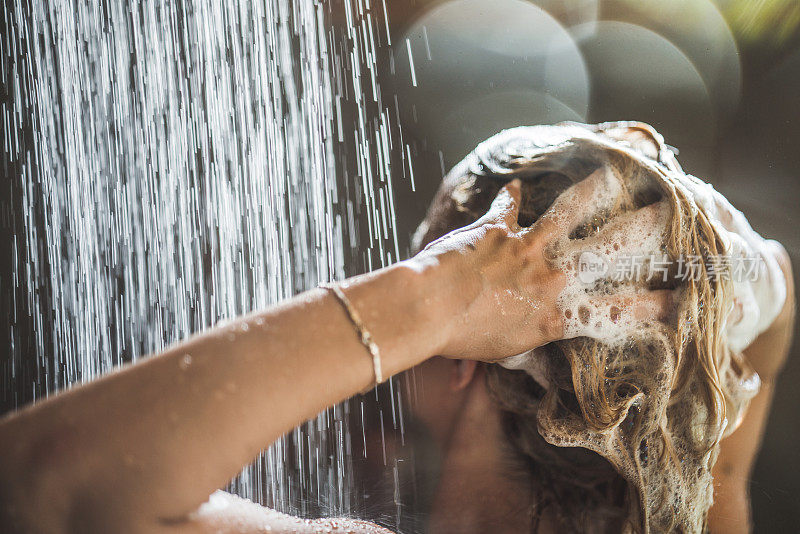 一个女人在淋浴下用香波洗头。