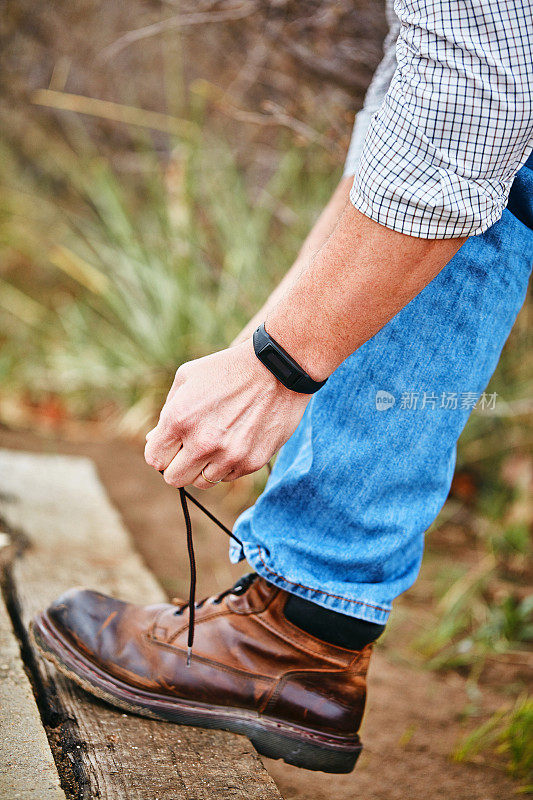 成年男性穿着休闲服装，用健身追踪器系鞋带