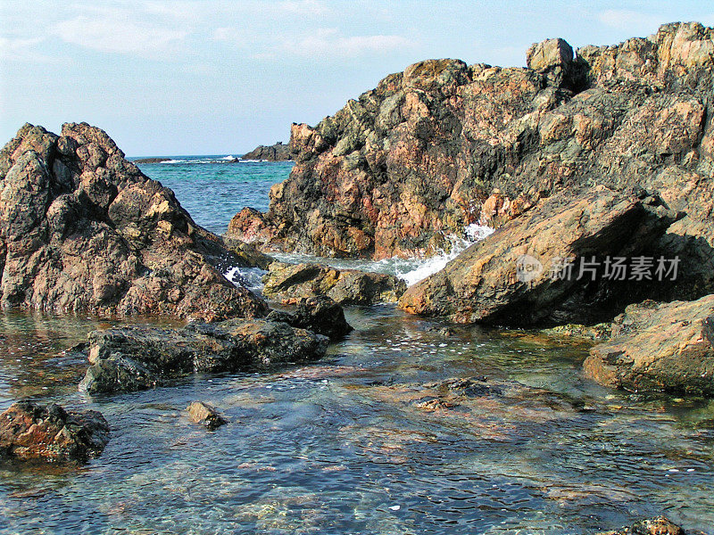 岩石嶙峋的海岸线，海浪轻轻拍打着岩石