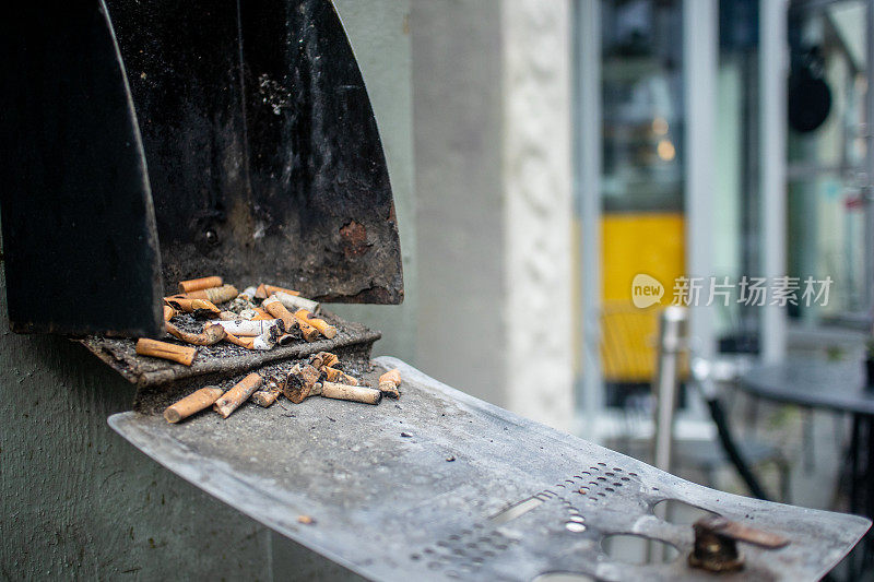街头咖啡馆外一个装满烟头的脏旧烟灰缸。强调了社会对这种习惯的偏见。